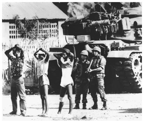 In the shadow of an American M-60 tank, two U.S. soldiers stand guard over three Grenadian prisoners. President Ronald Reagan ordered the invasion of Grenada in 1983 in order to oust its Marxist government. AP/WIDE WORLD PHOTOS.